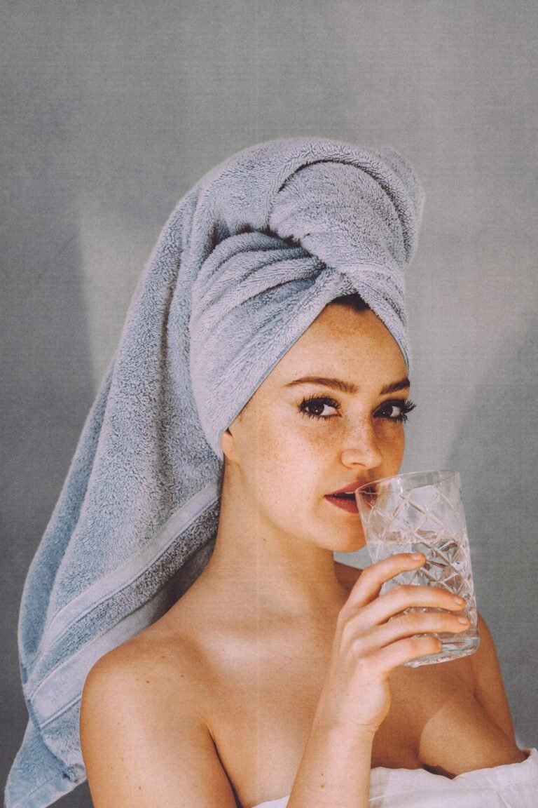 A woman with a towel turban on her head drinks from a glass.