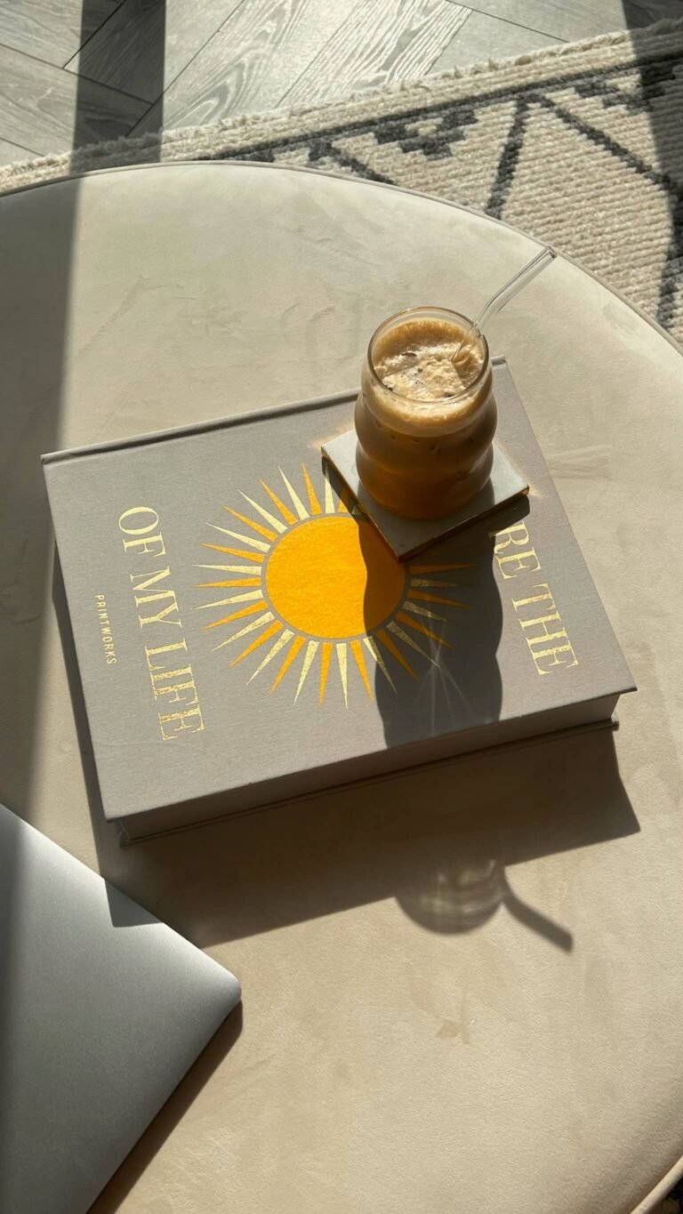 A book and an iced latte on a table in the sunshine.