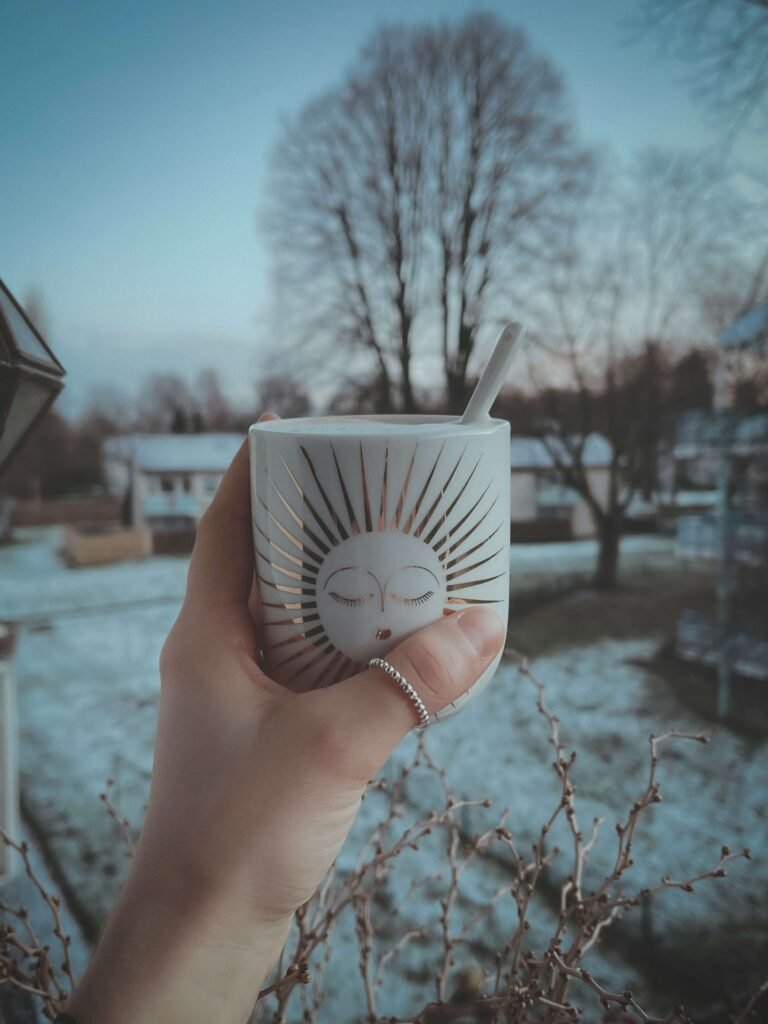 A female hand holding a cup in front of a snowy background.