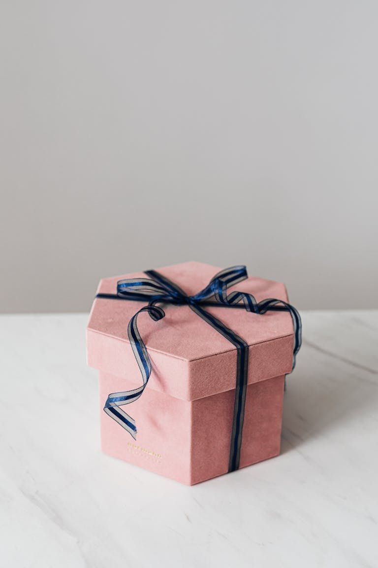A minimalist pink hexagon gift box with a navy ribbon on a marble surface, perfect for celebrations.