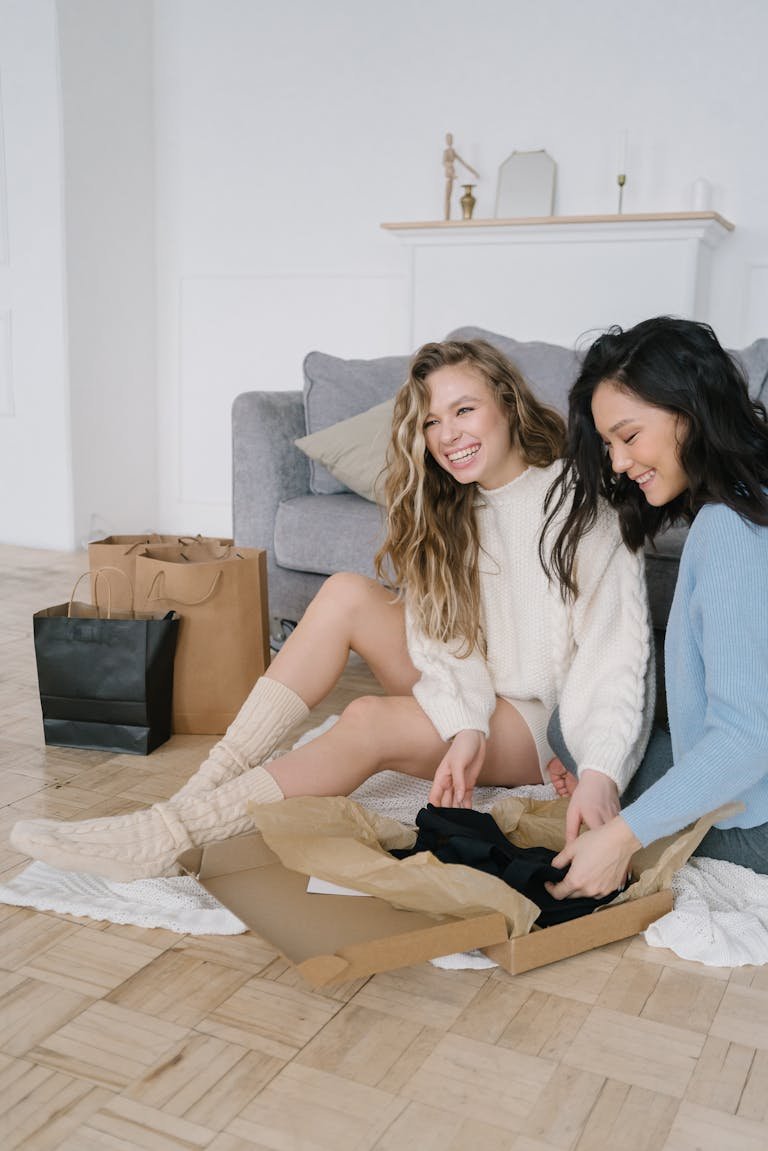 Two women happily unboxing a package at home, surrounded by shopping bags.